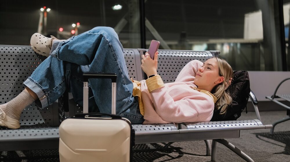 Young,Female,Traveler,Resting,On,Airport,Bench,With,Suitcase,And Cestovanie neplnoletých pasažierov bez rodičov: čo potrebujú mať pri sebe?