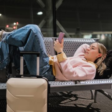 Young,Female,Traveler,Resting,On,Airport,Bench,With,Suitcase,And Cestovanie neplnoletých pasažierov bez rodičov: čo potrebujú mať pri sebe?