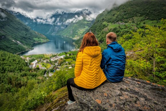 Couple,In,Blue,And,Yellow,Sitting,Over,Fjord,In,Norway. par s krasym vyhladom nad fjordom v norsku